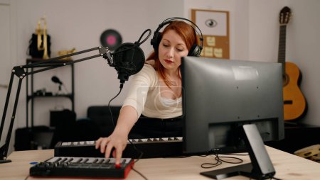 Foto de Young redhead woman musician playing piano keyboard at music studio - Imagen libre de derechos
