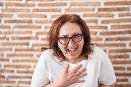 Photo for Senior woman with glasses standing over bricks wall smiling and laughing hard out loud because funny crazy joke with hands on body. - Royalty Free Image