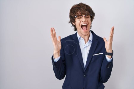 Téléchargez les photos : Hispanic business young man wearing glasses celebrating mad and crazy for success with arms raised and closed eyes screaming excited. winner concept - en image libre de droit