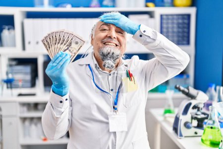 Photo for Middle age man with grey hair working at scientist laboratory holding money stressed and frustrated with hand on head, surprised and angry face - Royalty Free Image
