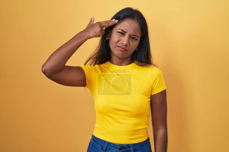 Photo for Young indian woman standing over yellow background shooting and killing oneself pointing hand and fingers to head like gun, suicide gesture. - Royalty Free Image