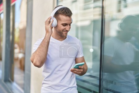 Téléchargez les photos : Young caucasian man listening to music standing at street - en image libre de droit
