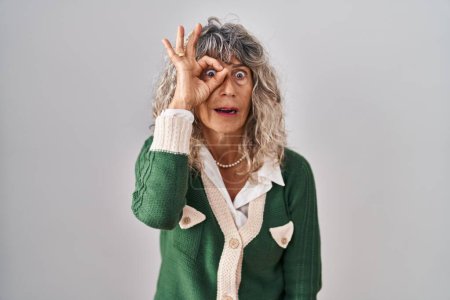 Photo for Middle age woman standing over white background doing ok gesture shocked with surprised face, eye looking through fingers. unbelieving expression. - Royalty Free Image