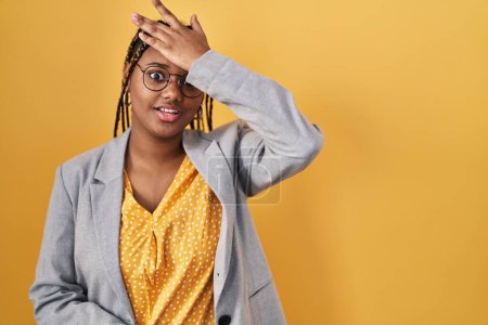 Téléchargez les photos : African american woman with braids standing over yellow background surprised with hand on head for mistake, remember error. forgot, bad memory concept. - en image libre de droit