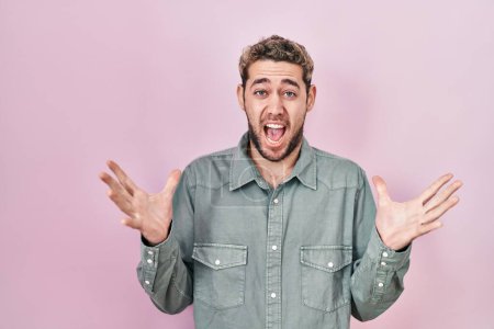 Téléchargez les photos : Hispanic man with beard standing over pink background celebrating crazy and amazed for success with arms raised and open eyes screaming excited. winner concept - en image libre de droit