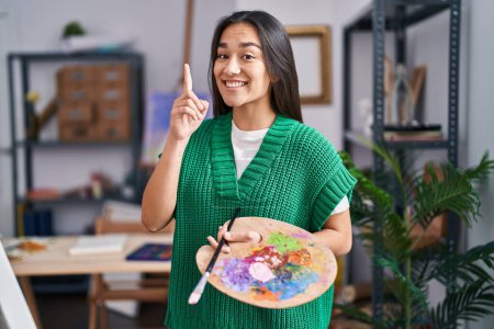 Foto de Young south asian woman holding painter palette surprised with an idea or question pointing finger with happy face, number one - Imagen libre de derechos