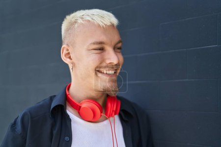 Téléchargez les photos : Jeune homme caucasien souriant confiant portant des écouteurs à la rue - en image libre de droit
