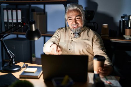 Photo for Middle age man with grey hair working at the office at night pointing to you and the camera with fingers, smiling positive and cheerful - Royalty Free Image
