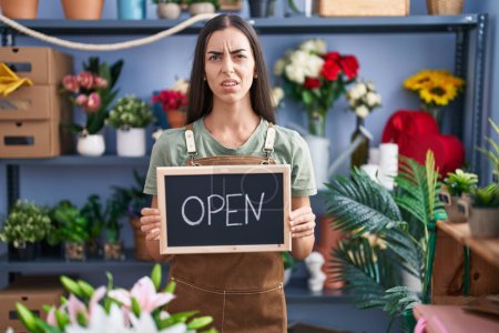 Photo for Young brunette woman working at florist holding open sign clueless and confused expression. doubt concept. - Royalty Free Image