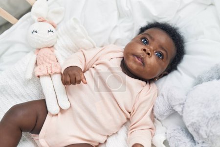 Téléchargez les photos : Bébé afro-américain couché sur le berceau avec une expression détendue dans la chambre - en image libre de droit