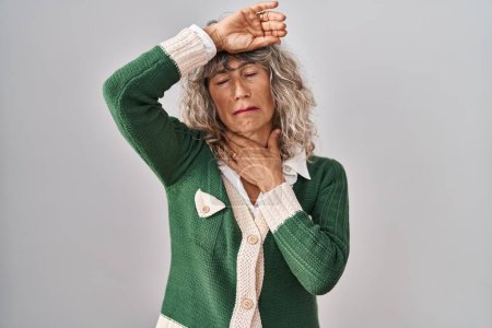 Foto de Middle age woman standing over white background touching forehead for illness and fever, flu and cold, virus sick - Imagen libre de derechos