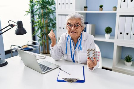 Photo for Senior woman with grey hair wearing doctor uniform holding prescription pills screaming proud, celebrating victory and success very excited with raised arm - Royalty Free Image