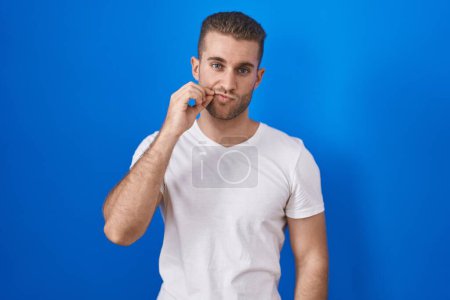 Photo for Young caucasian man standing over blue background mouth and lips shut as zip with fingers. secret and silent, taboo talking - Royalty Free Image