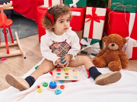 Téléchargez les photos : Adorable hispanic girl sitting on floor by christmas tree playing maths puzzle game at home - en image libre de droit