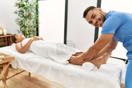 Photo for Latin man and woman wearing physiotherapy uniform having rehab session massaging legs at beauty center - Royalty Free Image