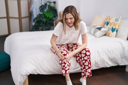 Téléchargez les photos : Young woman suffering for knee pain sitting on bed at bedroom - en image libre de droit
