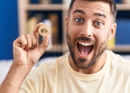 Foto de Hombre hispano guapo sosteniendo moneda criptomoneda tron celebrando logro con sonrisa feliz y expresión ganadora con la mano levantada - Imagen libre de derechos