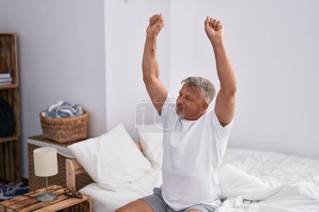 Téléchargez les photos : Middle age grey-haired man waking up stretching arms at bedroom - en image libre de droit