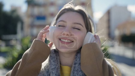 Téléchargez les photos : Jeune femme blonde souriante à l'écoute de musique au parc - en image libre de droit