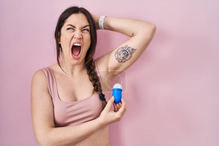 Téléchargez les photos : Jeune femme brune utilisant le rouleau sur le déodorant en colère et fou hurlant frustré et furieux, criant de colère. rage et concept agressif. - en image libre de droit