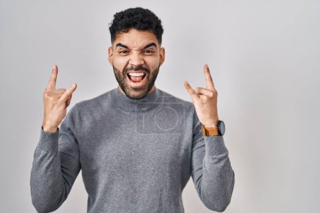 Foto de Hispanic man with beard standing over white background shouting with crazy expression doing rock symbol with hands up. music star. heavy music concept. - Imagen libre de derechos