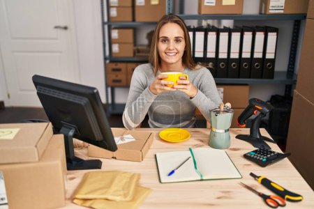 Téléchargez les photos : Jeune femme blonde ecommerce travailleur d'affaires boire du café au bureau - en image libre de droit