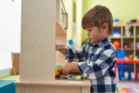 Téléchargez les photos : Adorable garçon hispanique jouant avec la cuisine de jeu debout à la maternelle - en image libre de droit