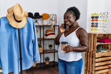 Téléchargez les photos : Jeune cliente afro-américaine parlant sur le smartphone et buvant du café au magasin de vêtements - en image libre de droit