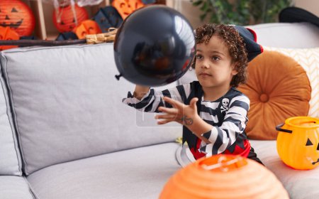 Foto de Adorable hispanic boy having halloween party playing with balloon at home - Imagen libre de derechos