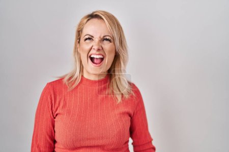 Photo for Blonde woman standing over isolated background angry and mad screaming frustrated and furious, shouting with anger. rage and aggressive concept. - Royalty Free Image