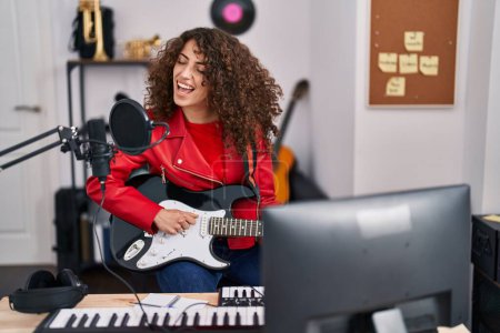 Téléchargez les photos : Jeune musicienne hispanique chantant une chanson jouant de la guitare électrique au studio de musique - en image libre de droit