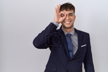 Photo for Young hispanic business man wearing suit and tie doing ok gesture with hand smiling, eye looking through fingers with happy face. - Royalty Free Image