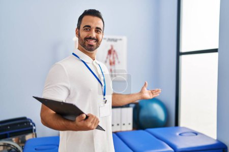 Photo for Young hispanic man physiotherapist smiling confident holding clipboard at rehab clinic - Royalty Free Image