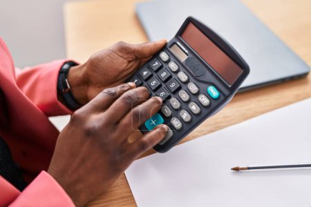 Téléchargez les photos : Femme afro-américaine travailleur d'affaires en utilisant une calculatrice au bureau - en image libre de droit