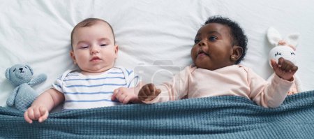 Téléchargez les photos : Deux adorables bébés souriants confiants allongés sur le lit dans la chambre - en image libre de droit