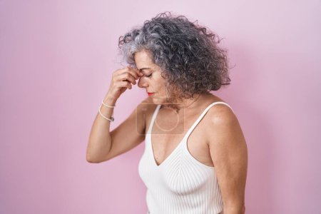 Photo for Middle age woman with grey hair standing over pink background tired rubbing nose and eyes feeling fatigue and headache. stress and frustration concept. - Royalty Free Image