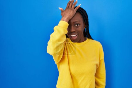 Photo for Beautiful black woman standing over blue background surprised with hand on head for mistake, remember error. forgot, bad memory concept. - Royalty Free Image
