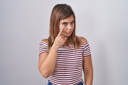 Foto de Young hispanic woman standing over isolated background pointing to the eye watching you gesture, suspicious expression - Imagen libre de derechos