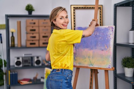 Foto de Young blonde woman artist smiling confident looking draw at art studio - Imagen libre de derechos