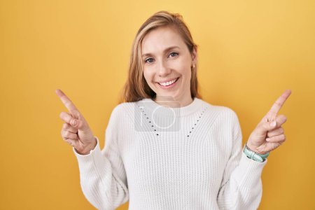 Foto de Mujer caucásica joven con suéter blanco sobre fondo amarillo sonriendo confiado señalando con los dedos a diferentes direcciones. espacio de copia para publicidad - Imagen libre de derechos