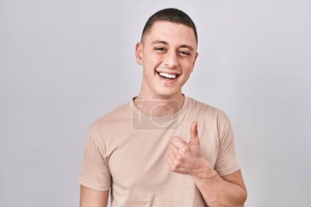 Photo for Young man standing over isolated background doing happy thumbs up gesture with hand. approving expression looking at the camera showing success. - Royalty Free Image