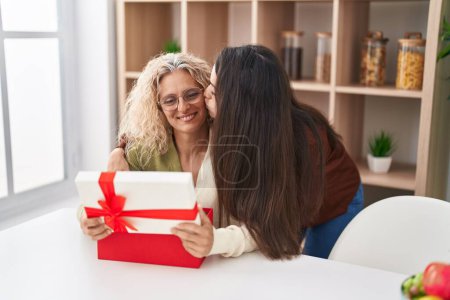 Foto de Dos mujeres madre e hija abrazándose la una a la otra sorpresa con regalo en casa - Imagen libre de derechos