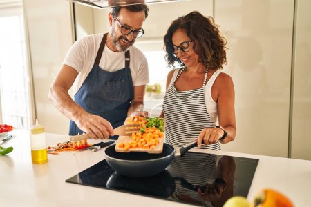 Photo for Middle age hispanic couple smiling confident pouring food on frying pan at kitchen - Royalty Free Image