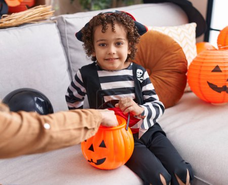 Téléchargez les photos : Adorable garçon hispanique ayant fête d'Halloween tenant panier de citrouille à la maison - en image libre de droit