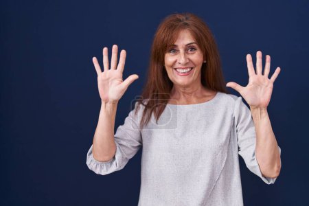 Téléchargez les photos : Femme d'âge moyen debout sur fond bleu montrant et pointant vers le haut avec les doigts numéro dix tout en souriant confiant et heureux. - en image libre de droit