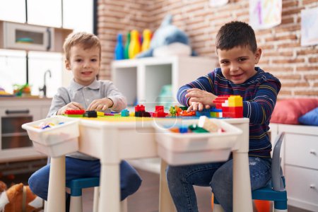 Foto de Dos niños jugando con bloques de construcción sentados en la mesa en el jardín de infantes - Imagen libre de derechos