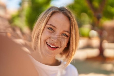 Téléchargez les photos : Jeune femme blonde souriante confiante faire selfie par caméra à la rue - en image libre de droit