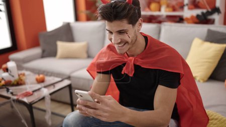 Photo for Young hispanic man wearing devil costume using smartphone at home - Royalty Free Image