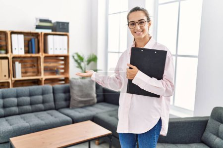 Photo for Young hispanic woman smiling confident holding clipboard standing at clinic - Royalty Free Image