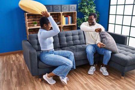 Photo for Man and woman couple fighting with cushion sitting on sofa at home - Royalty Free Image